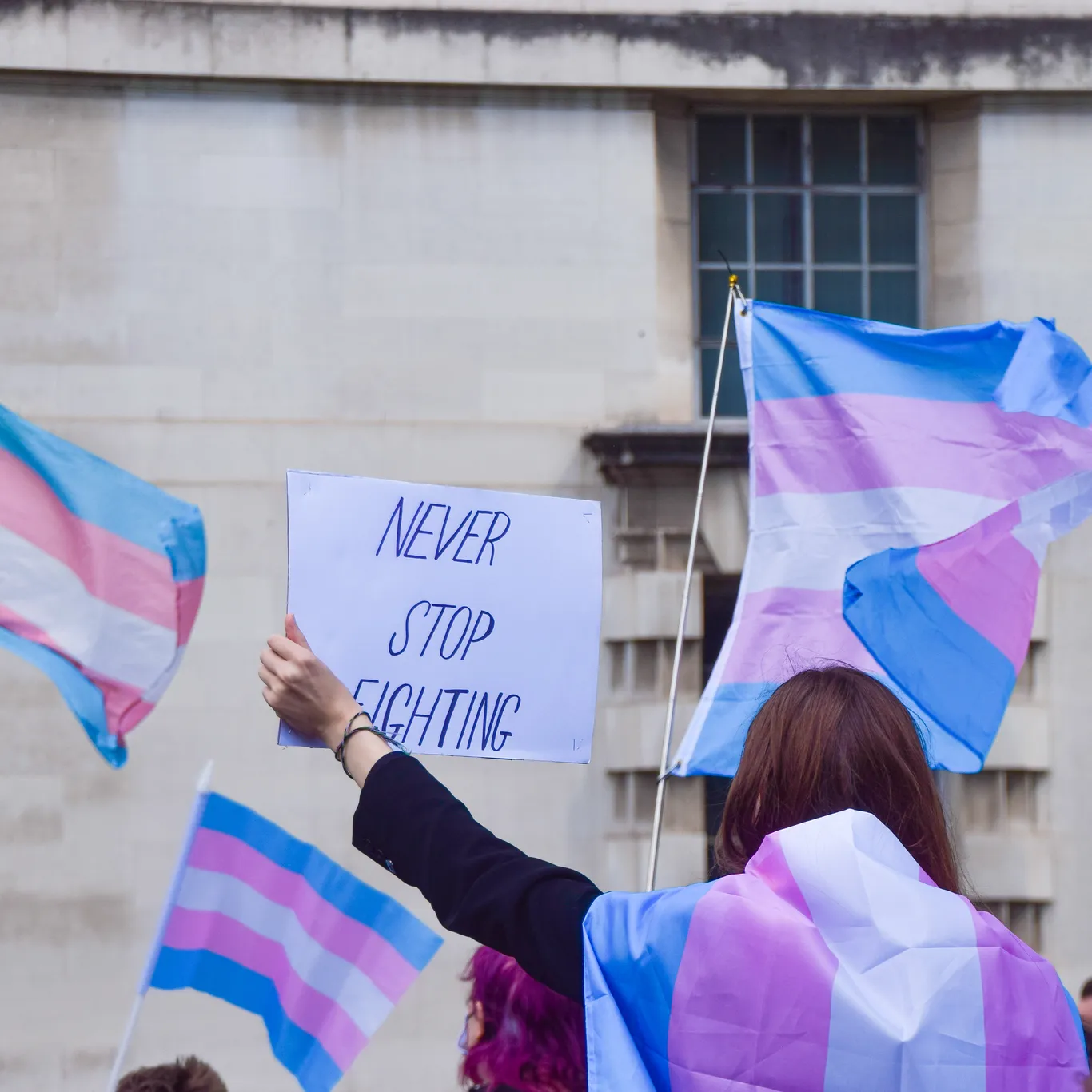 Trans activist zwaait met bord met daarop de tekst: ‘Never stop fighting’.