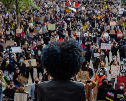 Een persoon met een afro-kapsel spreekt de menigte toe bij een BLM-protest