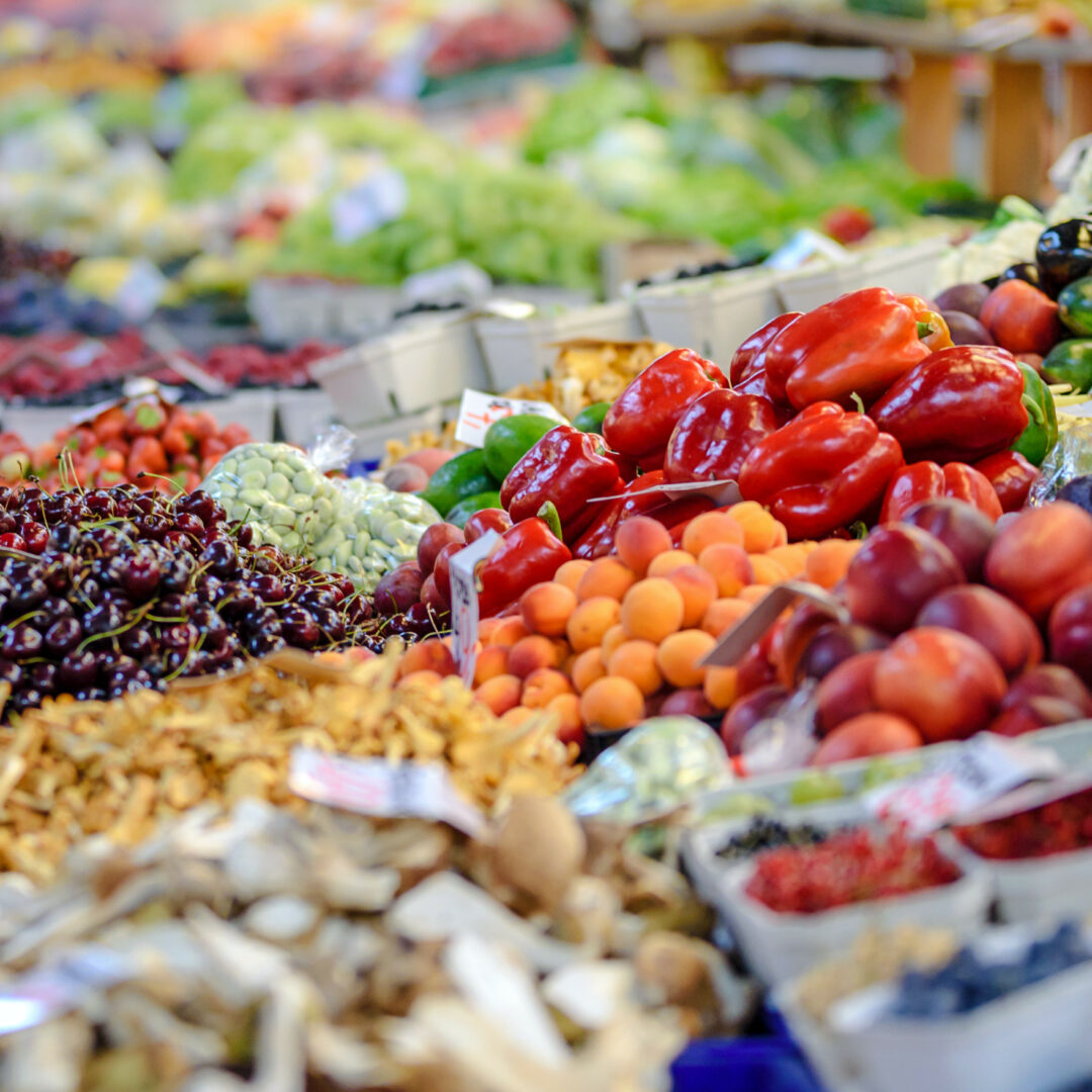 Op een uitgestalde marktkraam liggen allerlei soorten fruit en groenten: druiven, paprika, perzikken, aardappelen.