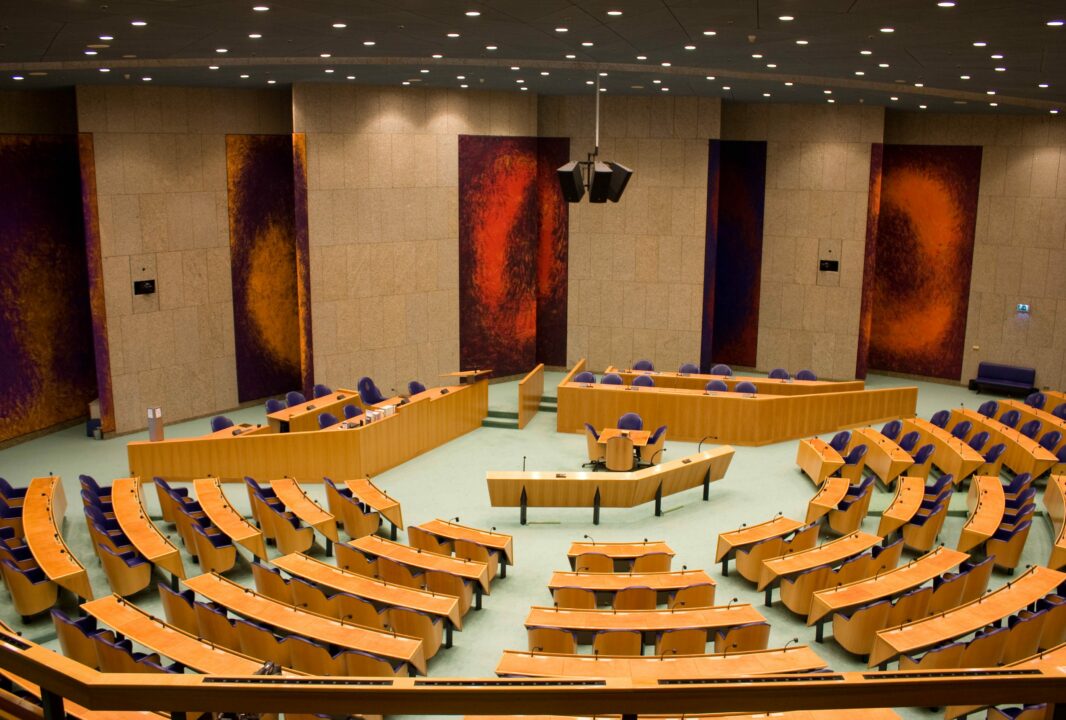 Dit is de pleniare zaal. De stoelen hebben de vorm van een tulp, het tapijt is groen als gras en het plafond heeft de blauwgrijze kleur van de Nederlandse lucht. De zaal moest ook iets van een theater hebben. Vandaar dat de stoelen zijn opgesteld in de halfronde vorm van een Romeins-Grieks theater. De roodpaarse wandpanelen met zeventien lagen olieverf onderstrepen het theatrale karakter.