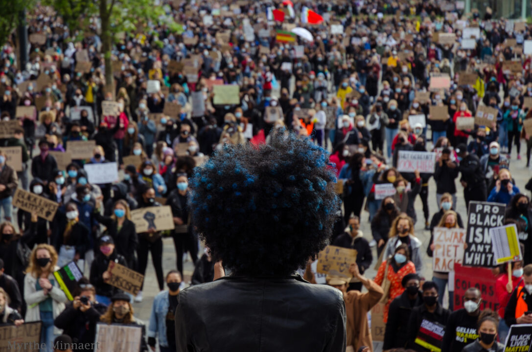 Een persoon met een afro-kapsel spreekt de menigte toe bij een BLM-protest