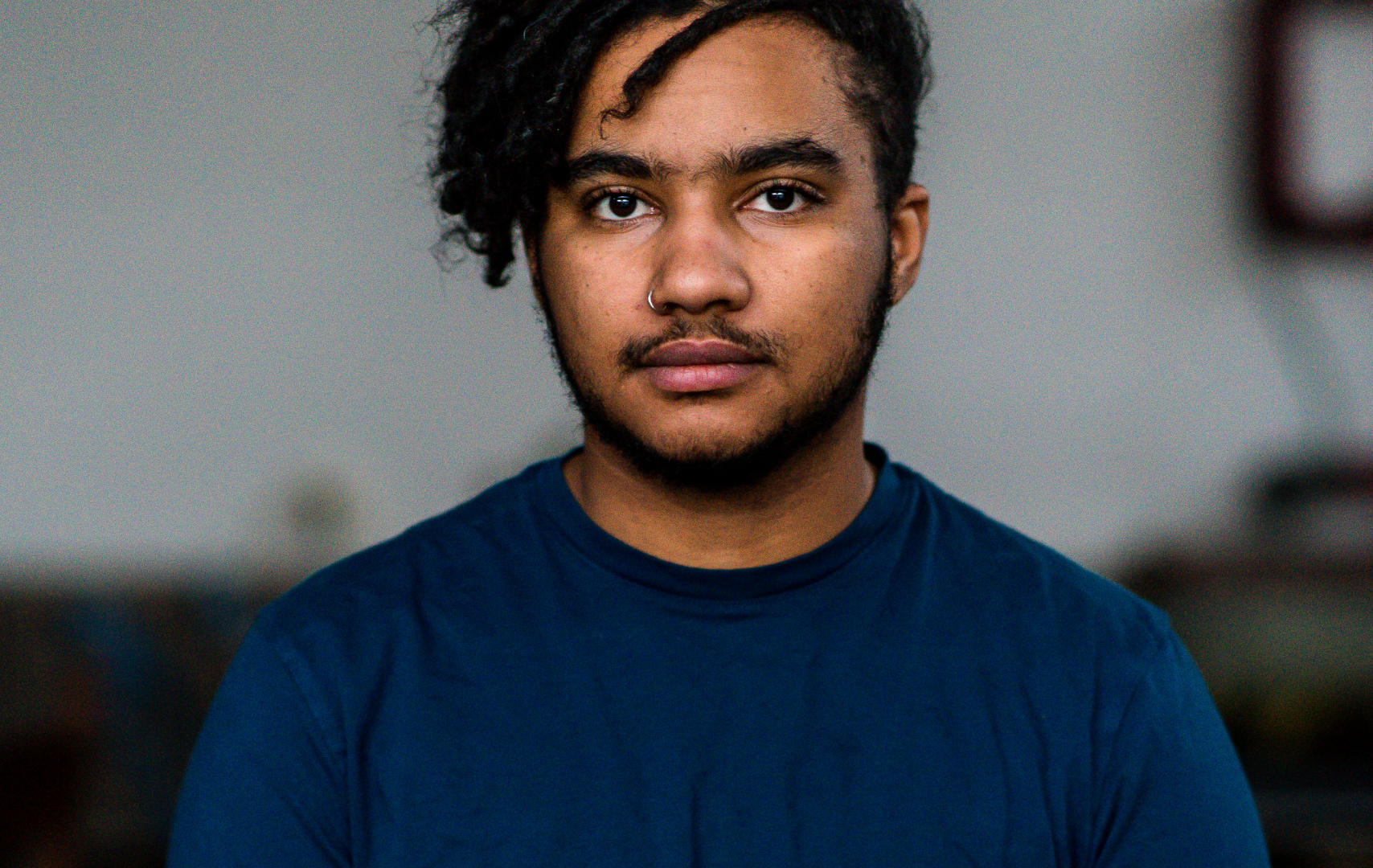 Portretfoto van Lennon. Hij is een zwarte man met een baard. Hij draagt een blauwe trui.