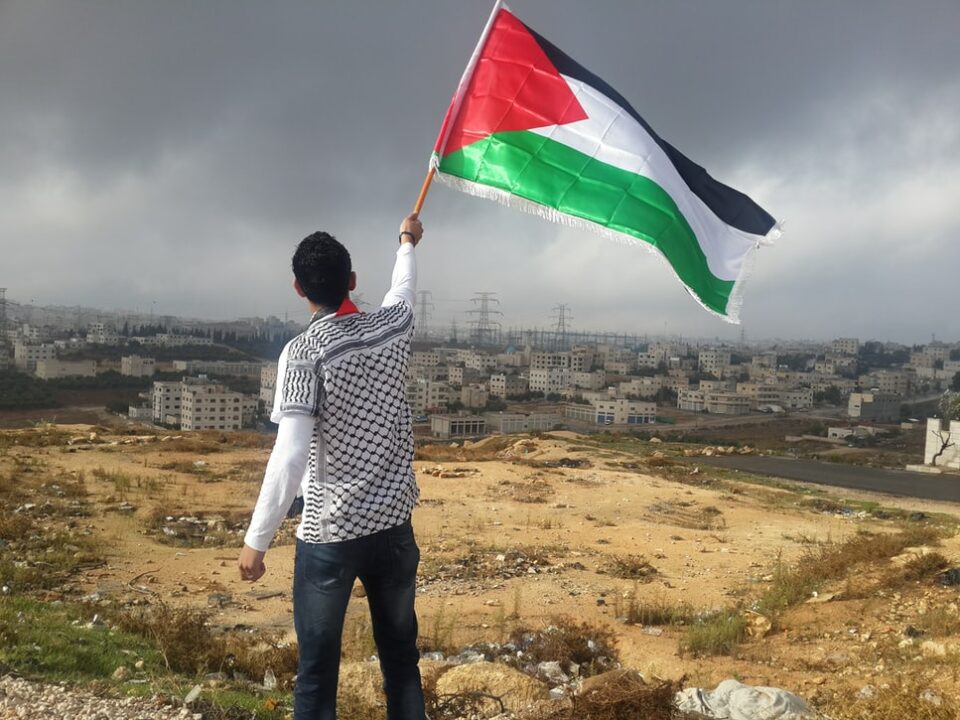 Persoon met een Palestijnse vlag voor een Israelische nederzetting.