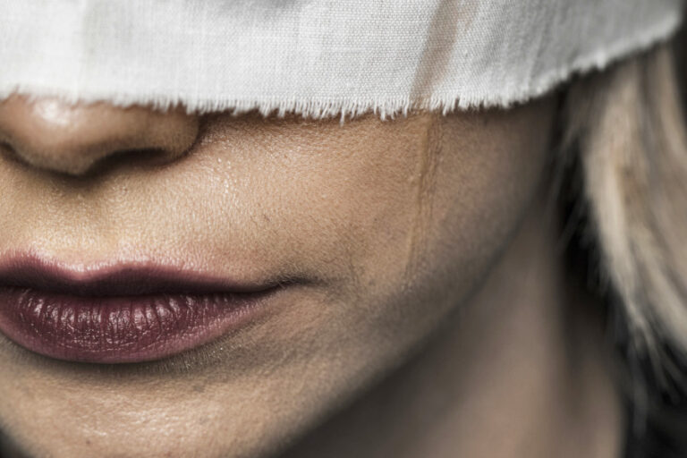 Close up van een vrouw met lipstick en een doek over haar ogen