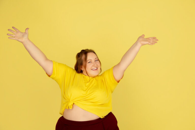 Dikke vrouw met geel shirt heft haar armen in trots gebaar