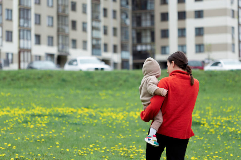 Vrouw met kind op de rug lopen over grasveld naar een grote flat