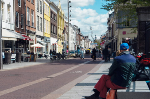 Foto van een typischs straat in Nederland met oude huizen, fietsers, wandelaars en mensen op een bankje